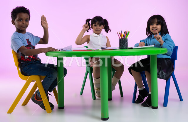Stationery and school tools for children, participation by raising the hand during class, pointing the index finger, classes and creative sessions in Saudi kindergartens, a portrait of Saudi Arab Gulf children in casual clothes raising their hands, a pink