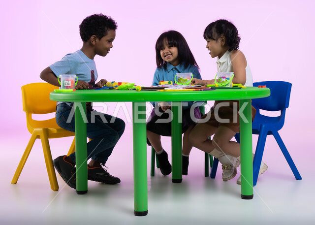 قضاء أوقات ممتعة ومفيدة في الروضة، نشاطات فنية تساعد على تنمية الجانب الإبداعي والابتكاري لدى الأطفال، تعلم صنع أشكال ومجسمات باستخدام العجينة الملونة، بورتريه لأطفال عرب خليجيين سعوديين يبدعون بنشاط اللعب بالمعجون الملون، خلفية وردية.