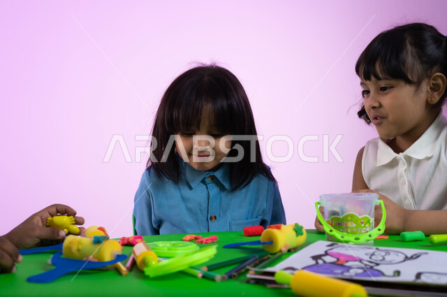 صنع أشكال باستخدام العجينة الملونة، أنشطة فنية وتعليمية تساعد على تعزيز الإبداع والمهارات الحركية والحسية الدقيقة عند الأولاد، بورتريه مقرب لأطفال عرب خليجيين سعوديين يبدعون بنشاط اللعب بالمعجون الملون في الروضة، خلفية وردية.