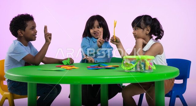المشاركة والتعاون بين أطفال الروضة في تعلم الرياضيات، تعلم الأرقام والأعداد العربية وأشكالها، نشاطات ترفيهية وتعليمية تساعد على تنمية القدرات الفكرية، بوتريه لأطفال عرب خليجيين سعوديين يرتدون الزي الكاجوال يتعلمون الحساب، خلفية وردية.