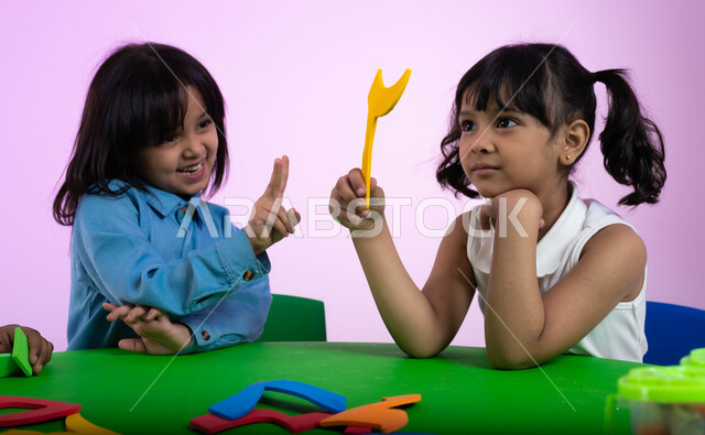 تعلم الأرقام والأعداد العربية وأشكالها، نشاطات ترفيهية وتعليمية للأطفال في الروضة، بوتريه لطفلتين عربيتين خليجيتين سعوديتين ترتديان الزي الكاجوال تتعلمان الحساب والرياضيات، خلفية وردية.