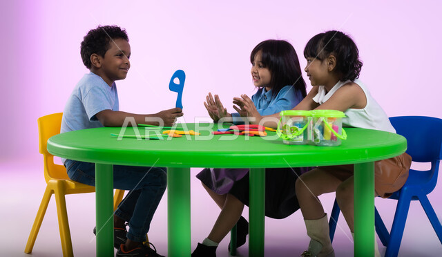 نشاطات ترفيهية وتعليمية تساعد على تنمية القدرات الفكرية، المشاركة والتعاون بين أطفال الروضة في تعلم الرياضيات، تعلم الأرقام والأعداد العربية وأشكالها، بوتريه لأطفال عرب خليجيين سعوديين يرتدون الزي الكاجوال يتعلمون الحساب، خلفية وردية.