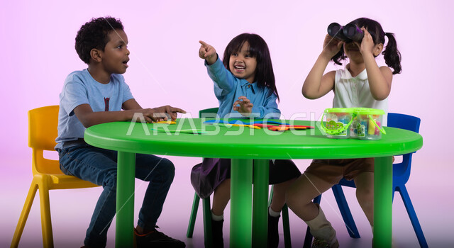 نظرة مستقبلية لدى الأولاد, بورتريه لأطفال عرب خليجيين سعوديين يرتدون الزي الكاجوال يجلسون في الروضة، طفلة سعودية تحمل بيدها المنظار ثنائي العينين، الإشارة إلى شيء ما ، حب الاستكشاف والمغامرة ، إيماءات وجه تدل على السعادة والدهشة، خلفية وردية. 