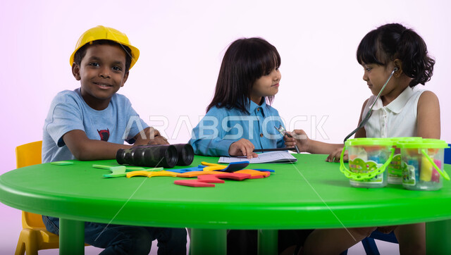 شرح وتعليم الوظائف والمهن المستقبلية للأطفال، الشغف بمهنة الهندسة منذ الطفولة، تعريف الأطفال في الروضة مفهوم الطب والرعاية الصحية، بورتريه لأطفال عرب خليجيين سعوديين يرتدون الزي الكاجوال، طفلة سعودية تقوم بالفحص بواسطة السماعة الطبية، خلفية زهرية.