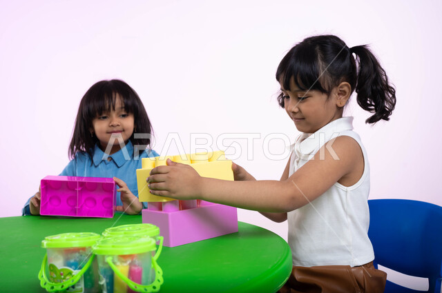 Places for incubating children, taking care of them and entertaining them, creativity and developing mental skills and abilities, facial gestures indicating happiness and pleasure, a close-up portrait of two Saudi Arabian Gulf girls dressed in casual clot