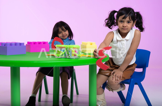 تعلم الأرقام والأعداد العربية وأشكالها، نشاطات ترفيهية وتعليمية للأطفال في الروضة، بوتريه لطفلتين عربيتين خليجيتين سعوديتين ترتديان الزي الكاجوال تنظران إلى الكاميرا بإيماءات تدل على السعادة والثقة بالنفس، خلفية وردية.