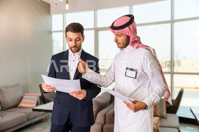 رجل اعمال سعودي خليجي في مقر الشركة مع السكرتير الخاص فيه يدير المهام اليومية ،ادارة الاعمال داخل مقر الشركة ، شركاء عمل ، متابعة الاهداف والخطط ، شركة سعودية ، بيئة العمل