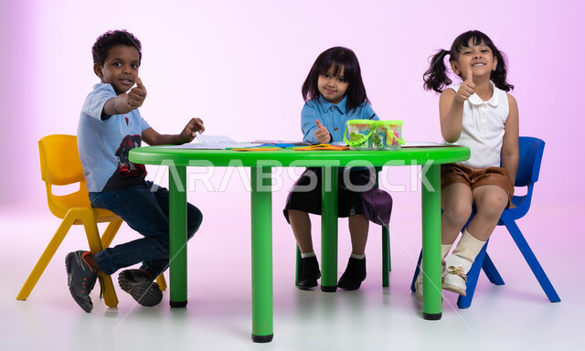 أماكن ترفيهية تعليمية للأطفال في المملكة العربية السعودية، النظر إلى الكاميرا، إيماءات وجه ويدين تدل على الرضا والقبول والإعجاب، بورتريه لأطفال عرب خليجيين سعوديين يرتدون الزي الكاجوال يشيرون بإصبعهم الإبهامي علامة لايك، خلفية ملونة.