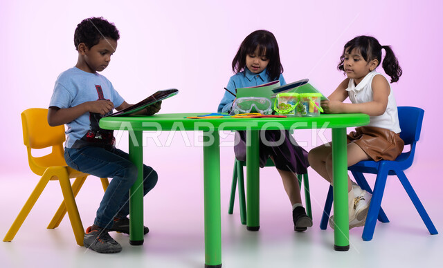 أماكن ترفيهية وتعليمية في المملكة العربية السعودية، مهارات وأنشطة تساعد على تنمية القدرات العقلية والذهنية، الاندماج والتركيز في التعلم، بورتريه لأطفال عرب خليجيين سعوديين يرتدون الزي الكاجوال يمارسون نشاط تهجئة الحروف، خلفية وردية.