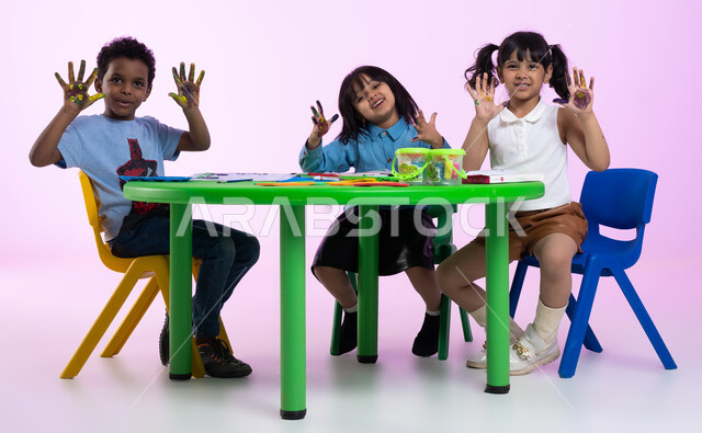 تقنيات الرسم لمرحلة ماقبل المدرسة، التعلم واكتساب المهارات منذ الصغر، أنشطة تساعد على التطور الفكري، إيماءات تدل على المتعة والسعادة، بورتريه لأطفال عرب سعوديين خليجيين يرتدون الزي الكاجوال يشيرون بأيديهم، طباعة الألوان المائية بكف اليد، خلفية وردية.