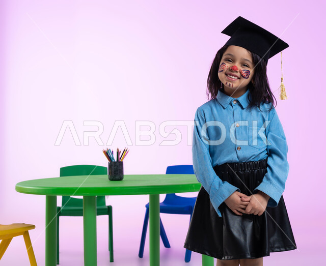 رسومات وجه للبنات تدل على الأنوثة واللطافة، الرسم بالألوان على وجوه الأطفال، بورتريه لفتاة عربية خليجية سعودية ترتدي قبعة التخرج، إيماءات وجه تدل على الحماس والسعادة بالنجاح في الروضة، خلفية وردية.