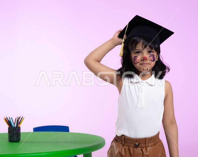 رسومات وجه للبنات تدل على الأنوثة واللطافة، الرسم بالألوان على وجوه الأطفال، بورتريه لطفلة عربية خليجية سعودية ترتدي الزي الكاجوال وقبعة التخرج من الروضة، إيماءات وجه تدل على الحزن والرغبة بالبكاء، خلفية وردية.