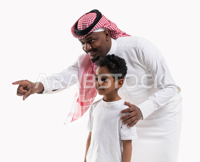 مفهوم تربية الابناء على الطريق الصحيح والاهتمام بهم، بورتريه لرجل عربي خليجي سعودي يرتدي  الثوب والشماغ السعودي برفقة ولده يشير بأصبعه للدلالة على شيء ما، لفت الانتباه لشيء معين, خلفية بيضاء