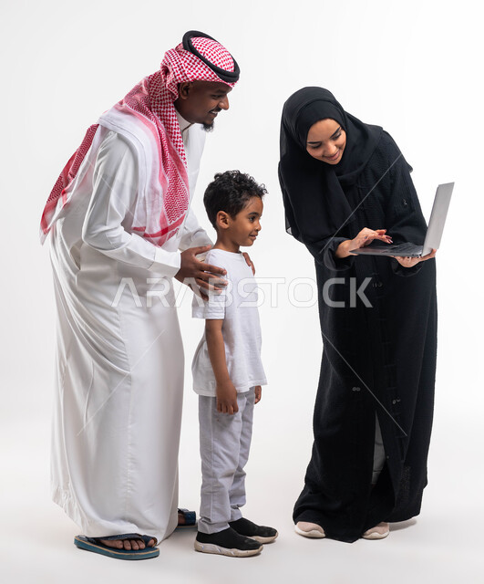 Encouraging and taking care of children, following online classes via a laptop, a portrait of a Saudi Arabian Gulf boy next to his parents doing distance learning with gestures of laughter and happiness, new news on social media, full-length body image, w