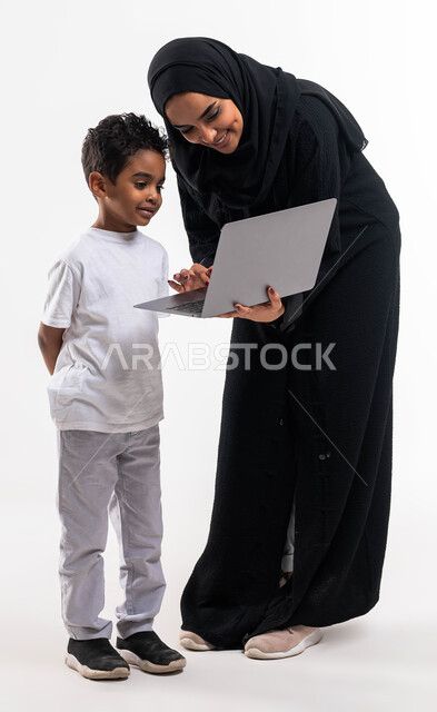 متابعة حصص الاونلاين عبر جهاز الحاسوب المحمول، بورتريه لولد عربي خليجي سعودي بجانب والدته يقوم بالتعلم عن بعد بإيماءات الضحك و السعادة، التسويق الالكتروني المنزلي، الاهتمام والاعتناء بالأبناء، أخبار جديده على مواقع التواصل الاجتماعي، خلفية بيضاء