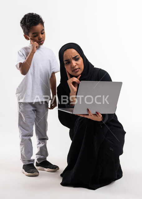 التعلم عن بعد، بورتريه لولد عربي خليجي سعودي بجانب والدته يقوم بمتابعة حصص الاونلاين عبر جهاز الحاسوب المحمول، إيماءات التفكير والتأمل، التسويق الالكتروني المنزلي، الاهتمام والاعتناء بالأبناء، أخبار جديده على مواقع التواصل الاجتماعي، خلفية بيضاء