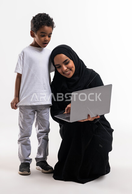 التعلم عن بعد، بورتريه لولد عربي خليجي سعودي بجانب والدته يقوم بمتابعة حصص الاونلاين عبر جهاز الحاسوب المحمول، إيماءات تدل على الصدمة والذهول، التسويق الالكتروني المنزلي، الاهتمام والاعتناء بالأبناء، أخبار جديده على مواقع التواصل الاجتماعي، خلفية بيضاء