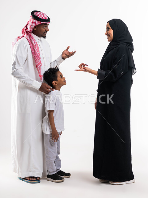 مفهوم التسلية والترفيه في حل الالغاز, تبادل الأسئله الثقافيه التعليميه مع العائلة، بورتريه لعائلة عربية خليجية سعودية مكونة من الأم والأب و الابن بإيماءات المرح والضحك، أنشطة ترفيهية ممتعة بين أفراد الأسرة، صورة الجسم بالطول الكامل، خلفية بيضاء
