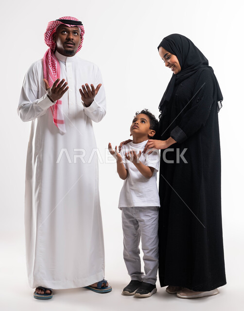 Praise and thanksgiving and asking for forgiveness, the advent of the holy month of Ramadan, a portrait of a Saudi Arabian Gulf man in traditional Saudi dress with his son standing next to the mother and raising their hands upward with gestures indicating