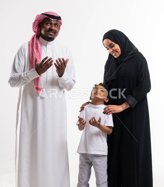 قدوم شهر رمضان المبارك، بورتريه لرجل عربي خليجي سعودي يرتدي الزي التقليدي السعودي مع ابنه يقفان بجانب الأم ويرفعان أيديهم الى الاعلى بإيماءات تدل على الدعاء، العبادة والتقرب الى الله تعالى، بناء مجتمع سعودي متنامي، الحمد والشكر وطلب المغفرة، خلفية بيضاء