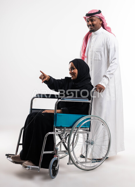 العطف والحنان والاهتمام  بالمرضى, الإهتمام والدعم لذوي الإحتياجات الخاصة ,بورتريه لإمرأه عربيه خليجية سعودية محجبة مقعدة تجلس على كرسي متحرك تشير الى شيء ما،  إيماءات تدل على المحبة والمودة ،تأمين أجهزة ومعدات تساعد في الحركة والتنقل، خلفية بيضاء