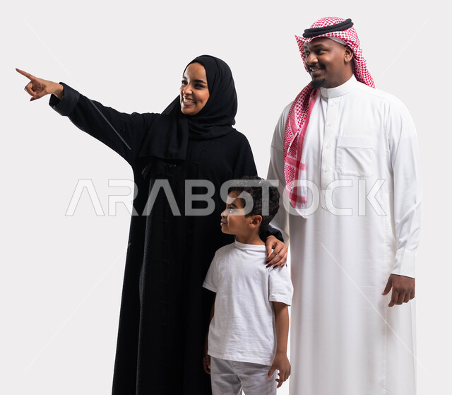الالتزام  بالقواعد والقوانين الأسريه، بورتريه لسيدة عربية خليجية سعودية محجبة برفقة ابنها وزوجها تشير بإصبعها الى شيء ما، قضاء الوقت مع الاهل والابناء، مفهوم الاستقرار العائلي ، ايماءات تدل على السعادة، خلفية بيضاء 