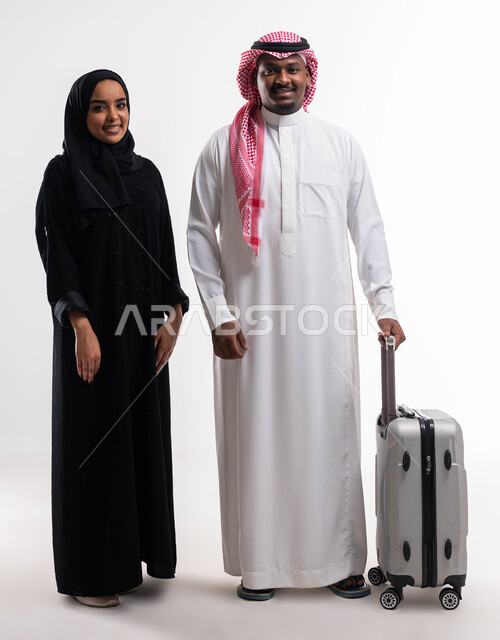 أنشطة سياحية ترفيهية، التأهب لرحلة سفر و قضاء اوقات ممتعة في العطلة مع الاهل، بورتريه لزوجان عربيان خليجيان سعوديان بإيماءات تدل على السعادة، المحافظة على تماسك الأسرة، صورة الجسم بالطول الكامل، خلفية بيضاء