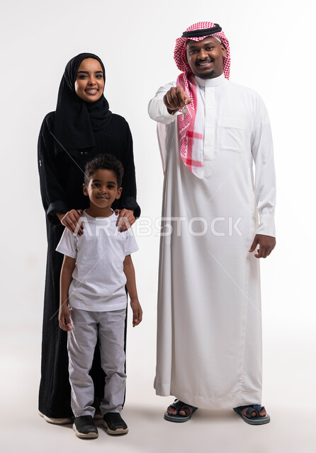 أساسيات العائلة  السعوديه السعيده، الالتزام  بالقواعد والقوانين الأسريه، بورتريه لرجل عربي خليجي سعودي مع عائلته يحمل بيده مفتاح المنزل الجديد، ايماءات تدل على السعادة والفرح ، الاستقرار العائلي في التمليك والاسكان، صورة الجسم بالطول الكامل، خلفية بيضاء