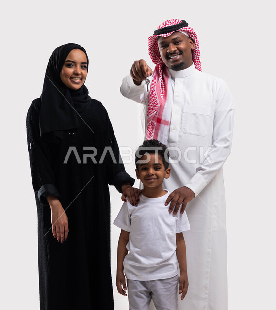 الالتزام  بالقواعد والقوانين الأسريه، بورتريه لرجل عربي خليجي سعودي مع عائلته يحمل بيده مفتاح المنزل الجديد، ايماءات تدل على السعادة والفرح ، الاستقرار العائلي في التمليك والاسكان، أساسيات العائلة  السعوديه السعيده، صورة الجسم بالطول الكامل، خلفية بيضاء