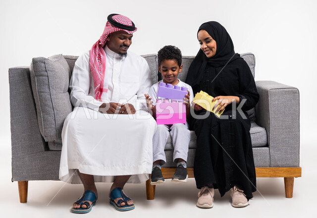 تعزيز المهارات الفكرية، بورتريه لعائلة عربية سعودية  تجلس على كنبة رمادية في غرفة المعيشة، ايماءات وجه تدل على السعادة، تنمية القدرات على الابتكار، انشطة ترفيهية مفيدة، قضاء أوقات ممتعه مع الاهل والأبناء، خلفية بيضاء