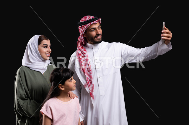 عرض فيديو بث مباشر، بورتريه لعائلة عربية سعودية خليجية تلتقط الصور التذكارية من خلال الهاتف المحمول، توثيق اللحظات العائلية السعيدة، الأجواء العائلية المليئة بالحب، مفهوم الأمان والإستقرار العائلي، المحافظة على الترابط الأسري، خلفية سوداء