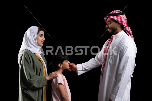 مفهوم الإهتمام والإعتناء بالأبناء، بورتريه لرجل سعودي خليجي عربي برفقة عائلته يقوم بمداعبة ابنته، الترابط الأسري والمحافظة على أمان وإستقرار العائلة، الأجواء العائلية المليئة بالحب، إيماءات السعادة والبهجة والسرور، خلفية سوداء