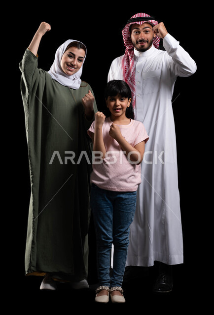 الترابط الأسري والمحافظة على الأمان والإستقرار العائلي، بورتريه لعائلة عربية خليجية سعودية تقوم برفع يدها لأعلى بحماس، إيماءات الفوز والنجاح والإنتصار وتحقيق الأهداف، قضاء أوقات عائلية ممتعة ومليئة بالحب، صورة الجسم بالطول الكامل، خلفية سوداء