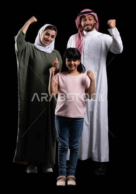 قضاء أوقات عائلية ممتعة ومليئة بالحب، بورتريه لعائلة عربية خليجية سعودية تقوم برفع يدها لأعلى بحماس، إيماءات الفوز والنجاح والإنتصار وتحقيق الأهداف، الترابط الأسري والمحافظة على الأمان والإستقرار العائلي، صورة الجسم بالطول الكامل، خلفية سوداء
