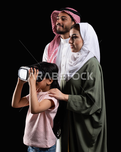 أنشطة تقنية ترفيهية مسلية، الإستمتاع بمشاهدة الأفلام ومحاكاة العالم الإفتراضي، بورتريه لفتاة عربية سعودية خليجية برفقة والديها ترتدي نظارات الواقع الإفتراضي (في آر) ثلاثية الإبعاد، مفهوم الإهتمام والإعتناء بالأبناء، خلفية سوداء