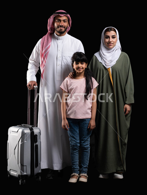المحافظة على أمان وإستقرار الأسرة، بورتريه لرجل سعودي خليجي عربي مع زوجته وابنته يمسك حقيبة الأمتعة وينظرون إلى الكاميرا، الإستعداد لقضاء الإجازة الصيفية والذهاب في رحلة سفر ممتعة، الأجواء العائلية المليئة بالحب، صورة الجسم بالطول الكامل، خلفية سوداء