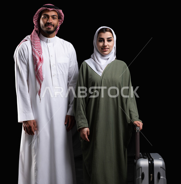Successful married life, portrait of a smiling Gulf Saudi Arabian couple, gestures indicating happiness, a woman holding a luggage bag, getting ready to spend the summer vacation and going on an enjoyable travel trip, black background
