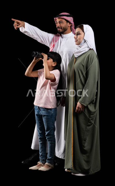 الأهداف والطموحات والرؤية المستقبلية، بورتريه لفتاة عربية خليجية سعودية رفقة والديها تنظر من خلال الناظور لرؤية الأشياء البعيدة، الإشارة لشيء ما بهدف لفت الإنتباه، تشجيع الأبناء على الإستكشاف والمغامرة، صورة الجسم بالطول الكامل، خلفية سوداء