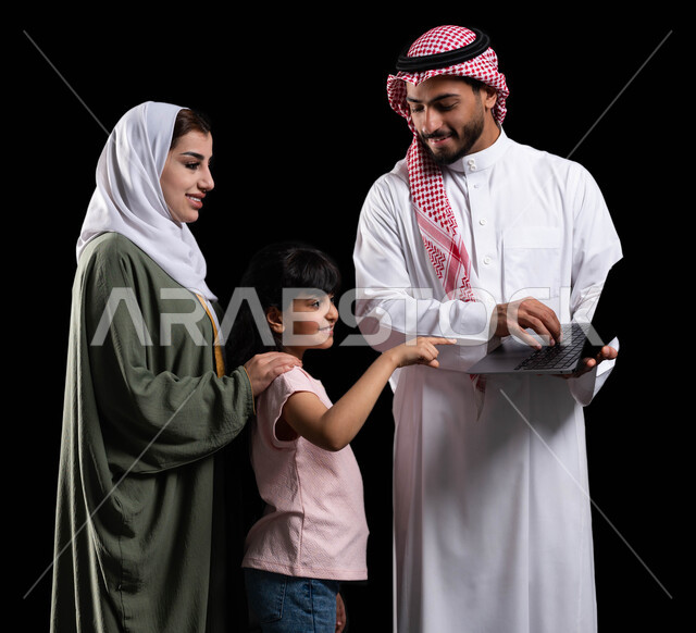 مفهوم الإهتمام والإعتناء بالعائلة، بورتريه لرجل عربي سعودي خليجي يحمل اللابتوب ويقف برفقة زوجته وابنته، الأجواء العائلية المليئة بالحب والترابط والإستقرار، متابعة حصص الأونلاين وإجراء مكالمة فيديو من خلال الحاسوب المحمول، خلفية سوداء