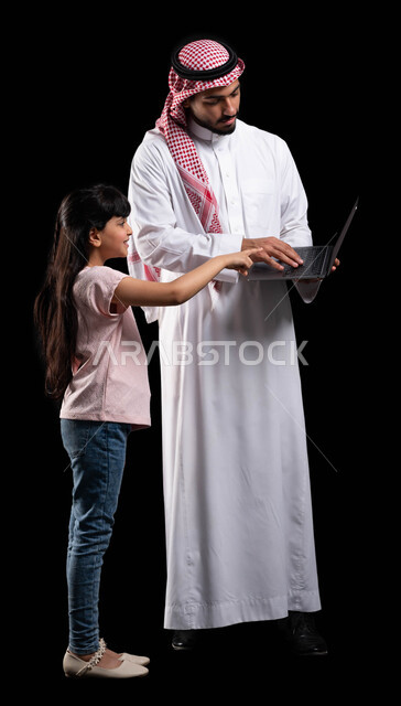 متابعة حصص الأونلاين من خلال الحاسوب المحمول، بورتريه لرجل عربي خليجي سعودي يقوم بتعليم ابنته إستخدام اللابتوب، الترابط الأسري والمحافظة على أمان وإستقرار العائلة، مفهوم الإهتمام والإعتناء بالأبناء، صورة الجسم بالطول الكامل، خلفية سوداء