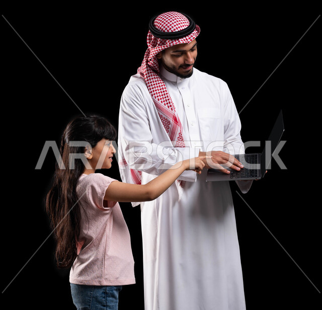 مفهوم الإهتمام والإعتناء بالأبناء، متابعة حصص الأونلاين من خلال الحاسوب المحمول، بورتريه لرجل عربي خليجي سعودي يقوم بتعليم ابنته إستخدام اللابتوب، الترابط الأسري والمحافظة على أمان وإستقرار العائلة، خلفية سوداء