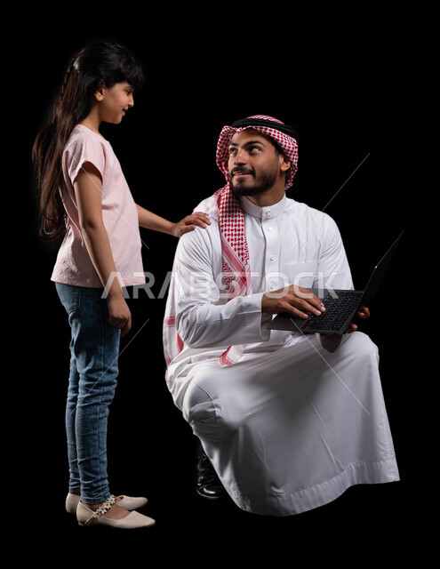 التسوق الإلكتروني وتصفح الإنترنت من خلال الحاسوب المحمول، بورتريه لرجل عربي خليجي سعودي يقوم بتعليم ابنته إستخدام اللابتوب، الترابط الأسري والمحافظة على أمان وإستقرار العائلة، مفهوم الإهتمام والإعتناء بالأبناء، صورة الجسم بالطول الكامل، خلفية سوداء
