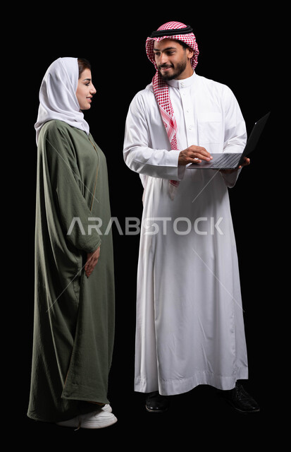 ايماءات وجه سعيدة, صورة الجسم بالطول الكامل, فريق عمل يقومون في التعاون والتشارك في إنجاز الأعمال, مناقشة وتنظيم الاعمال, بورتريه لرجل أعمال عربي خليجي سعودية يحمل الحاسوب المحمول بجانبه موظفة عربية خليجية سعودية, خلفية سوداء