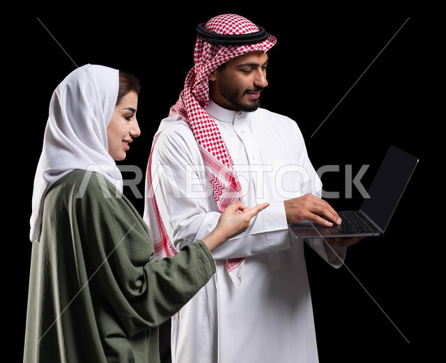 متابعة الاهداف والخطط في السعودية, فريق عمل يقومون في التعاون والتشارك في إنجاز الأعمال, النظر و الإشارة إلى شيء ما في الحاسوب, مناقشة وتنظيم الاعمال, بورتريه لرجل أعمال عربي خليجي سعودية يحمل الحاسوب المحمول بجانبه موظفة عربية خليجية سعودية, خلفية سوداء