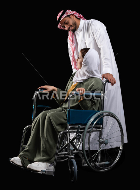 ايماءات البشاشه والمعامله الحسنه, الإخلاص  والعطف والحنان بين الأزواج،  زوج عربي خليجي سعودي يرتدي الزي السعودي يقوم بمساعدة زوجته من ذوي الاحتياجات الخاصه، مفهوم  العنايه ورعاية المرضى والمعاقين ، الاهتمام بالجانب النفسي والجسدي للمقعدين، خلفية سوداء