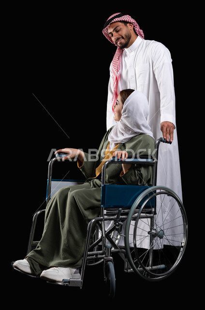 خلفية سوداء, الإخلاص  والعطف والحنان بين الأزواج، زوج عربي خليجي سعودي يرتدي الزي السعودي يقوم بمساعدة زوجته من ذوي الاحتياجات الخاصه، مفهوم  العنايه ورعاية المرضى والمعاقين ، الاهتمام بالجانب النفسي والجسدي للمقعدين، ايماءات البشاشه والمعامله الحسنه