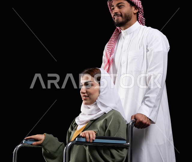 مساعدة مرضى ذوي الإعاقة الحركية على التنقل بسهولة, إمرأة عربية سعودية خليجية محجبة من ذوي الاحتياجات الخاصة تقدر مساعدة زوجها, ايماءات السعادة والتفاؤل بالحياة المستقبلية, خلفية سوداء, شعور ذوي الهمم بالراحه والطمأنينه في بيئتهم