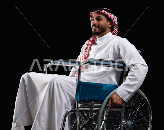 Gestures of happiness and optimism in the future life, maintaining activity and physical health by moving the hands during movement, a smiling Saudi Arabian man sitting in a wheelchair, using wheelchairs for people with disabilities to help move and move
