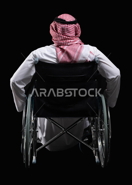 مريض يجلس على كرسي متحرك، تأمين اجهزة ومعدات تساعد بالحركة والتنقل، العنايه بأصحاب الهمم وتأمين احتياجاتهم الخاصة، صورة من الخلف لرجل عربي سعودي خليجي يرتدي الزي السعودي من ذوي الاحتياجات الخاصه، شعور المعاقين بالإنتماء والتقدير والإحترام في السعوديه، خلف