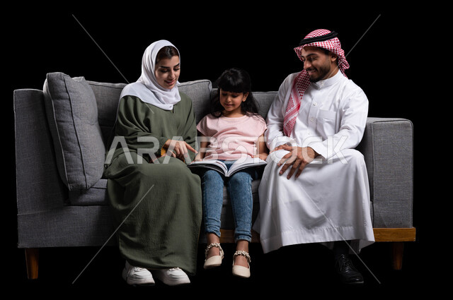 الأجواء العائلية المليئة بالحب والترابط والاستقرار, دور العائلة في تنمية ميول الأبناء, بورتريه لأسرة عربية خليجية سعودية تقوم بمساعدة ابنتهم على التعلم في المنزل, الجلوس على الكنبة في غرفة المعيشة وقضاء وقت ممتع في قراءة القصص المفيدة, خلفية سوداء
